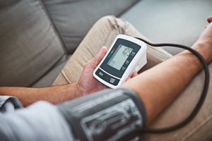 man doing a reading of his blood pressure with a blood pressure monitor while being seated on a couch at home